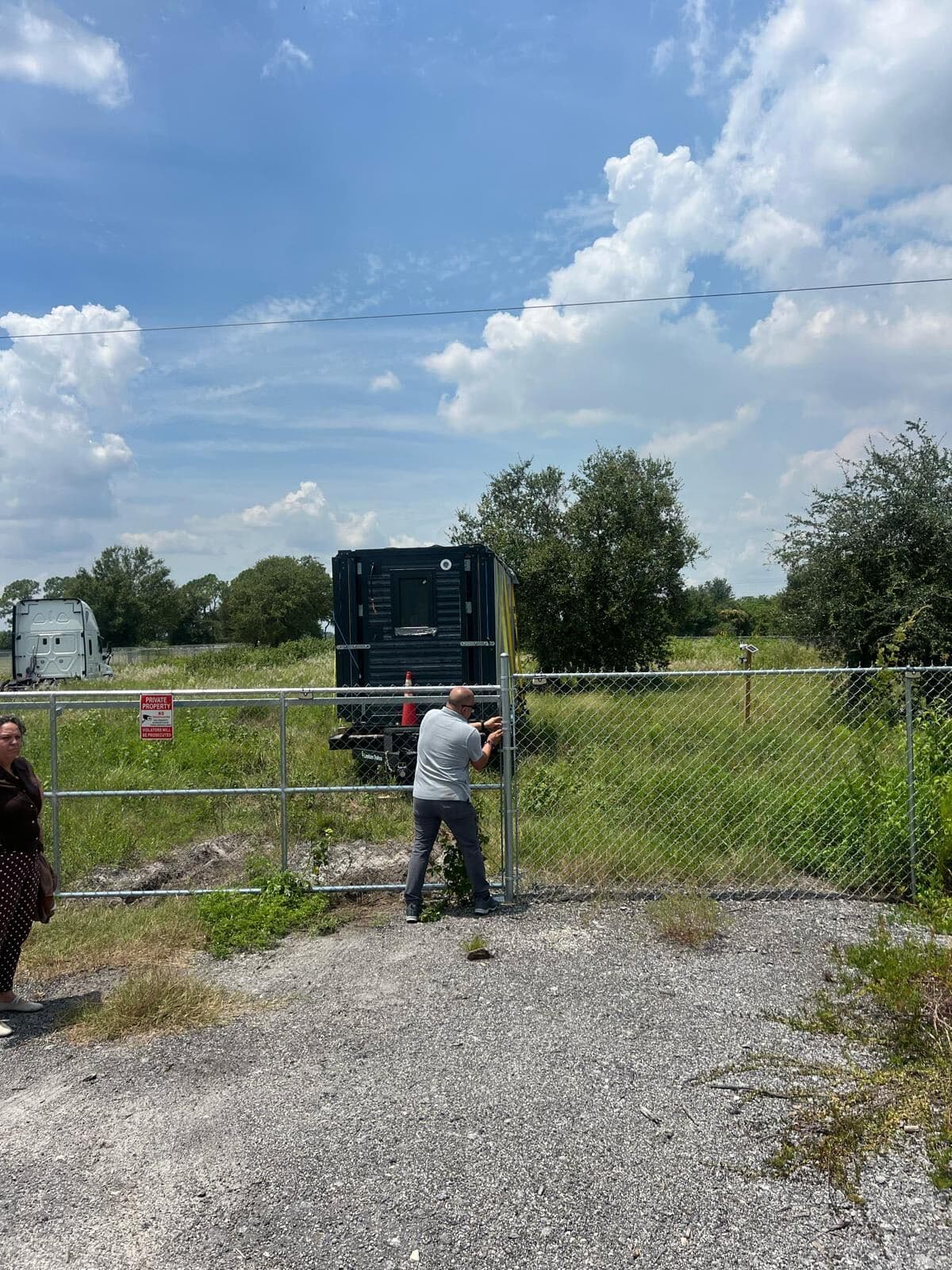 A dark steel PLAD OMNI unit on its delivery trailer, parked on a cleared lot behind a chain-link gate.